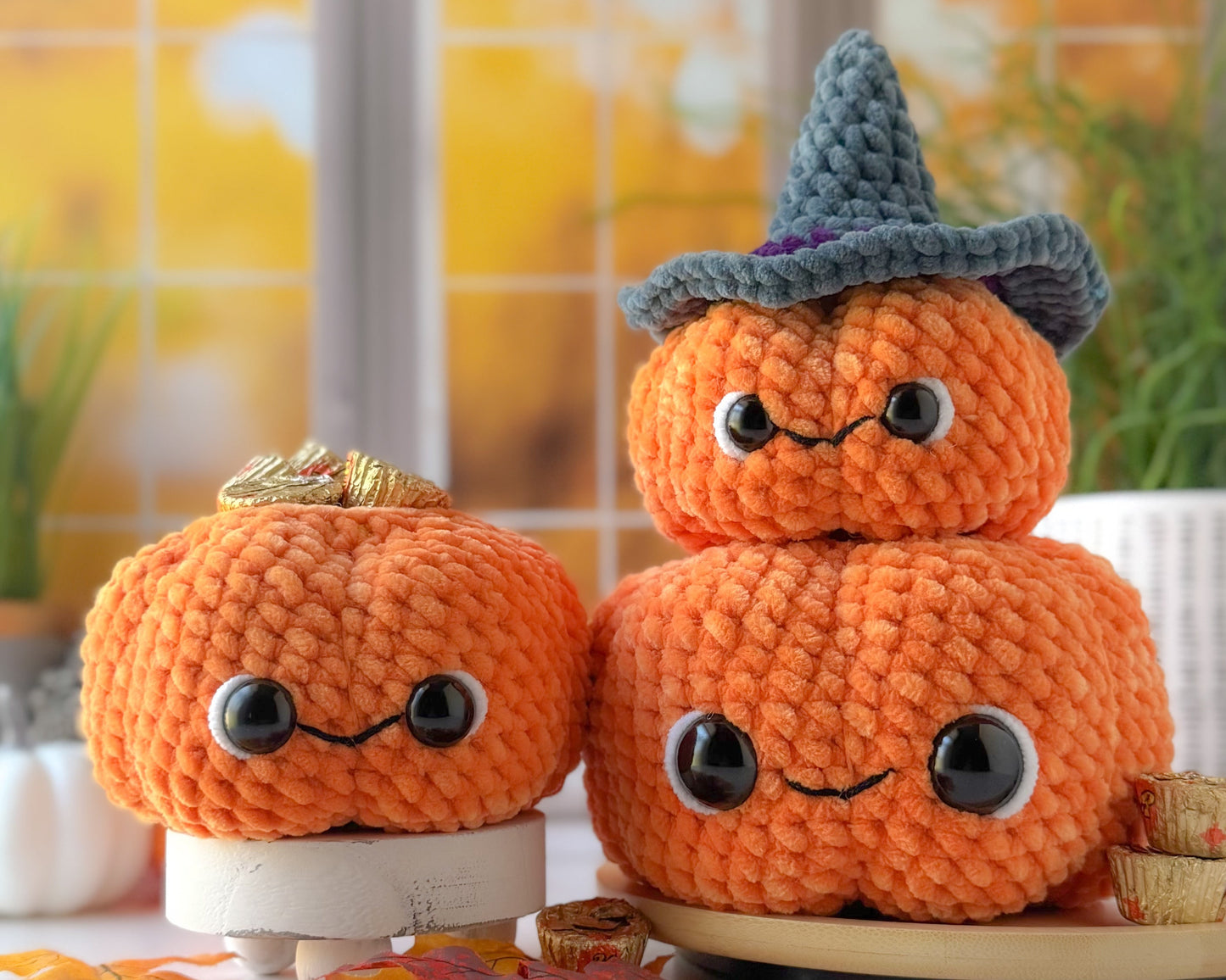 Three crocheted pumpkins with faces and a witch hat on a table with a blurred background.