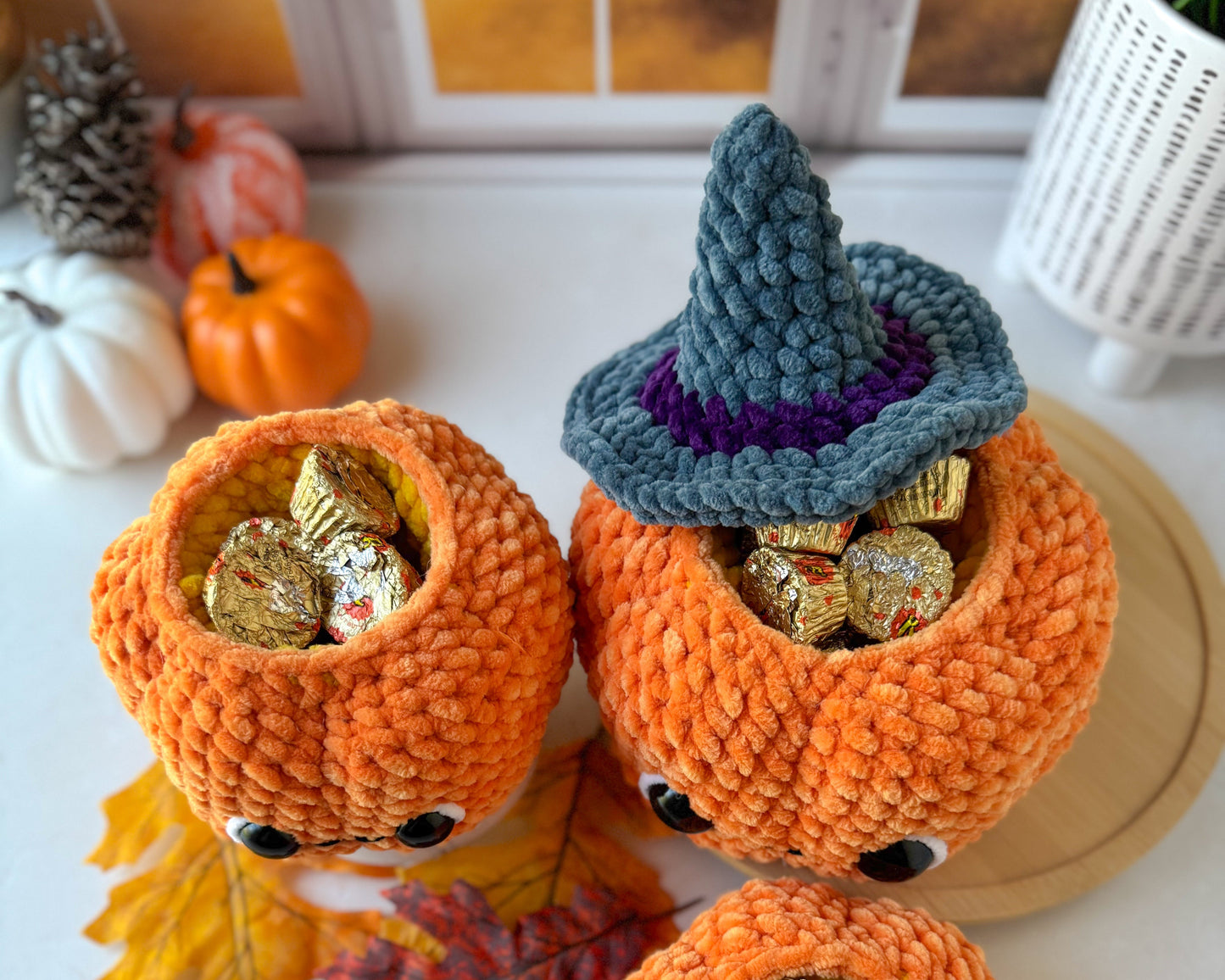 crochet pumpkins with candy and a witch hat on a white surface with autumn leaves.