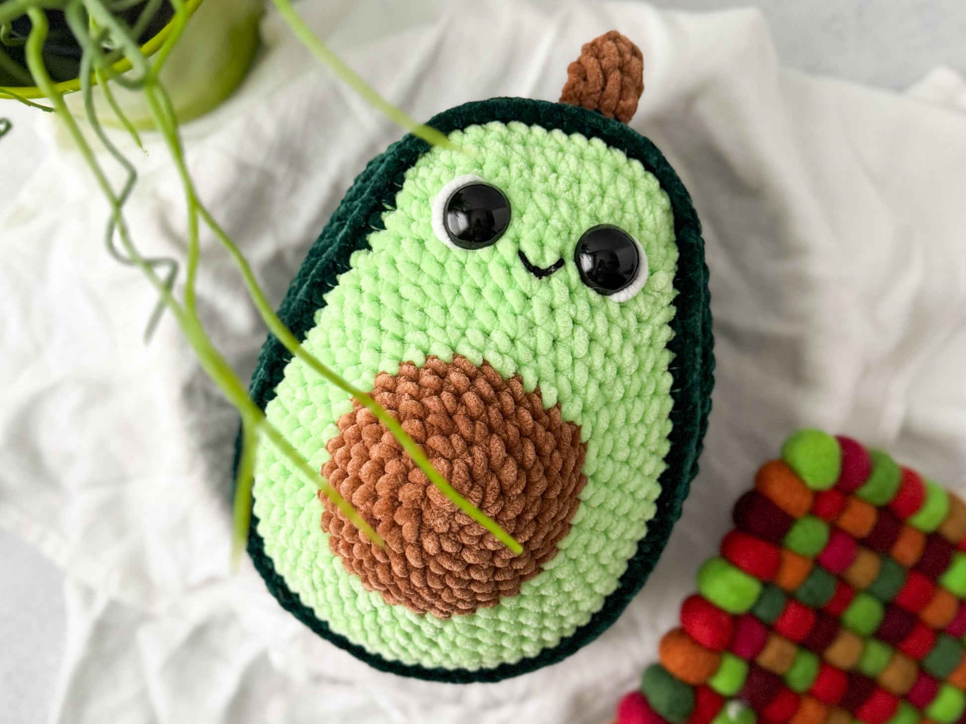 Crocheted avocado with a smiling face on a white fabric background