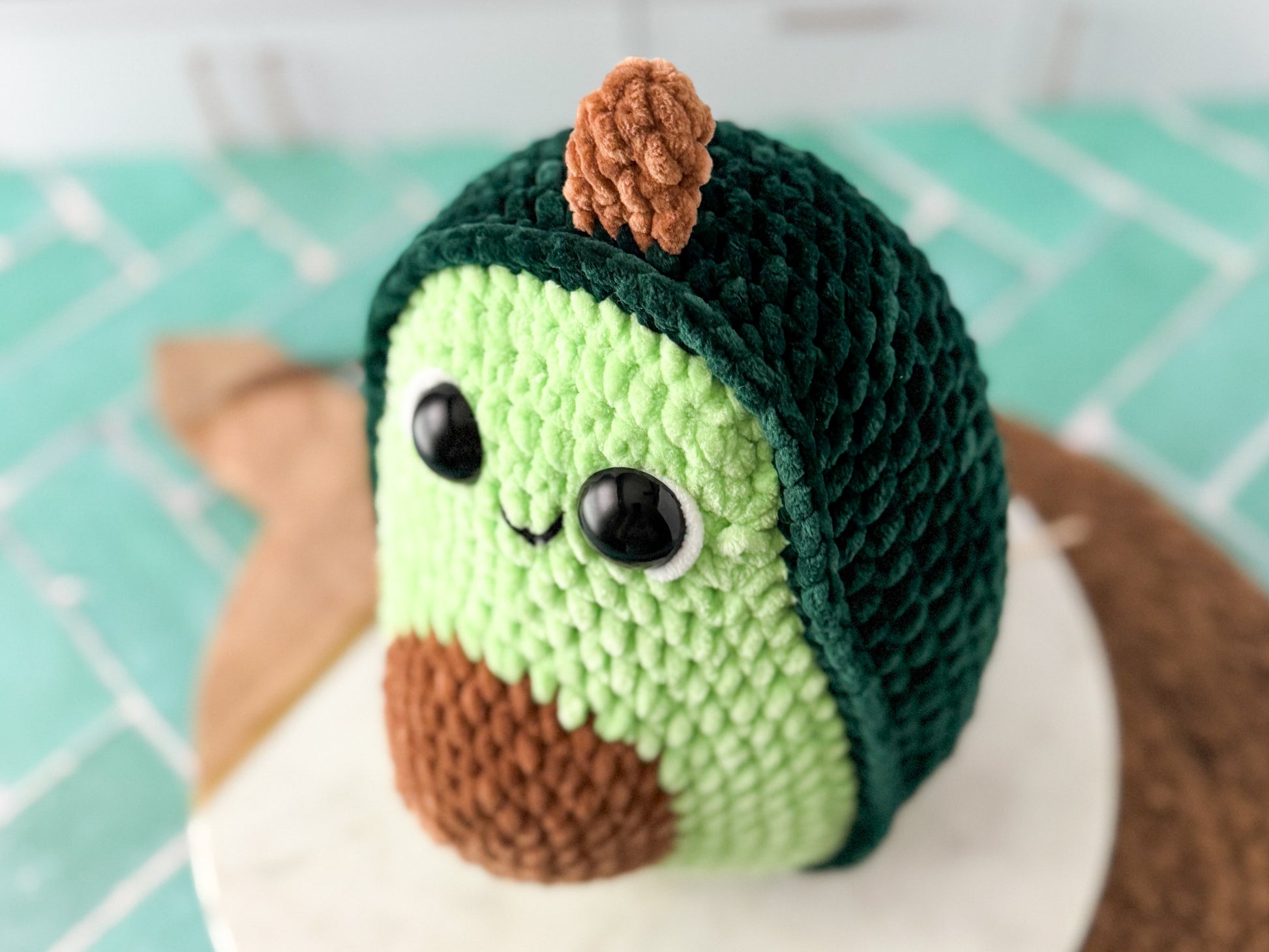 Crocheted avocado with a green body and brown seed on a white plate.