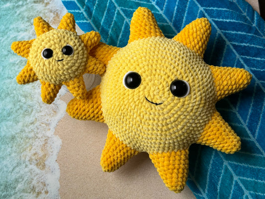 Two yellow crochet sun toys on a beach with blue water and sand.