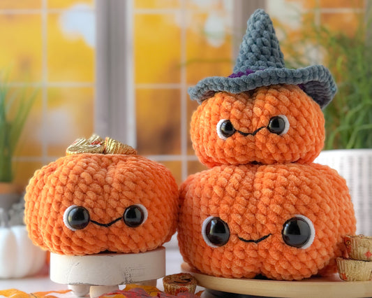 Three crocheted pumpkins with faces and a witch hat on a table with a blurred background.