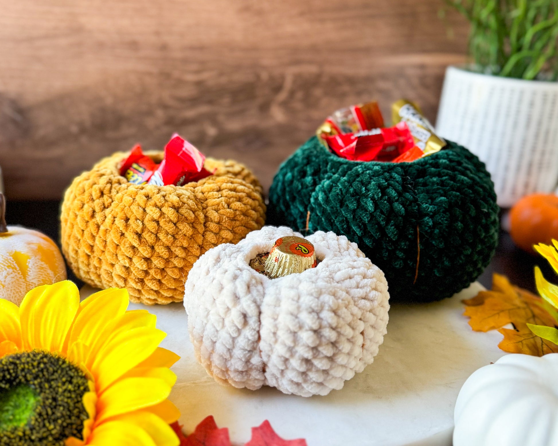 Decorative crochet pumpkins with candles on a wooden surface with autumn leaves and flowers.