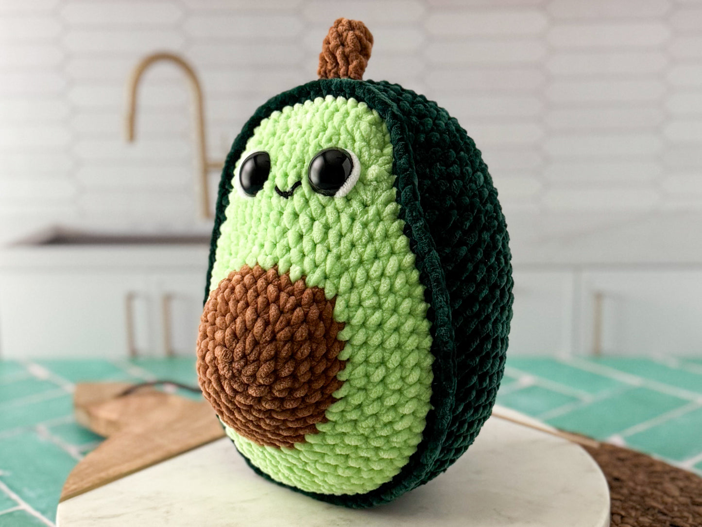 Crocheted avocado plush toy on a kitchen counter with a white tiled wall background