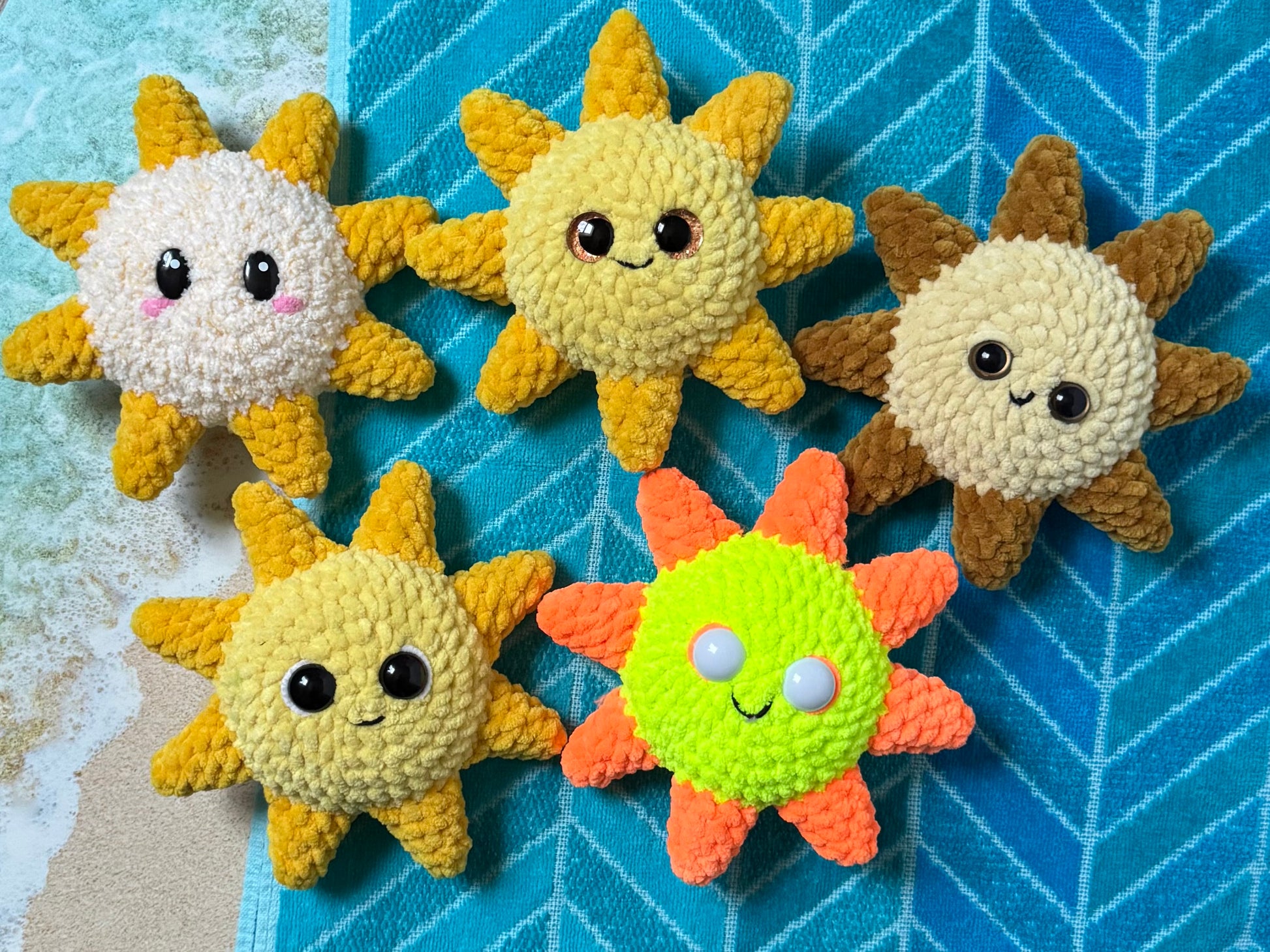 Five colorful sun-shaped plush toys on a blue textured beach towel background