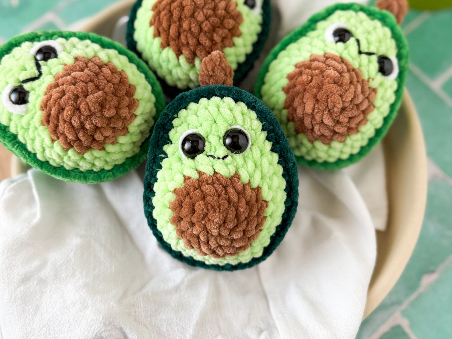 Four crocheted avocados with faces on white fabric.