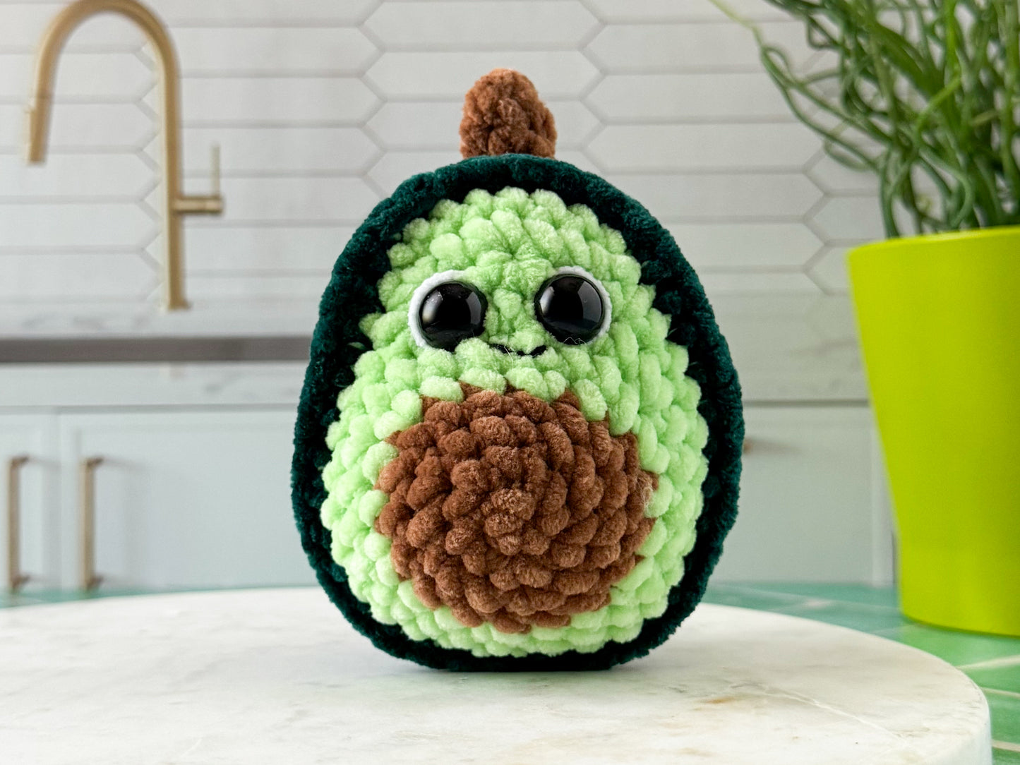 Crocheted avocado toy on a kitchen counter with a plant in the background