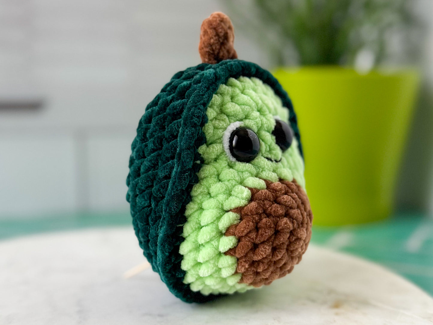 Crocheted avocado toy with a smiling face on a marble surface.