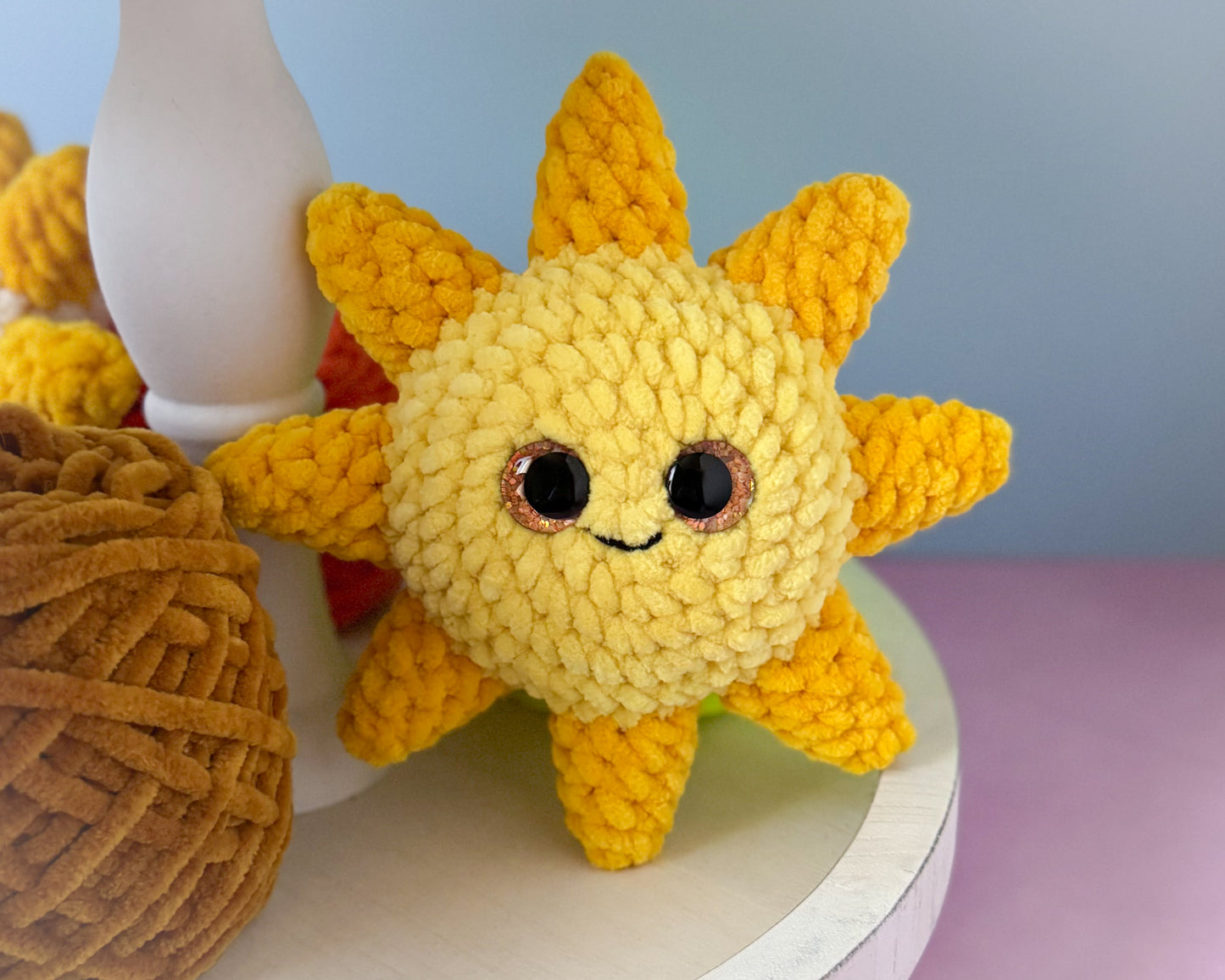 Crocheted sun-shaped toy with a face on a light surface.