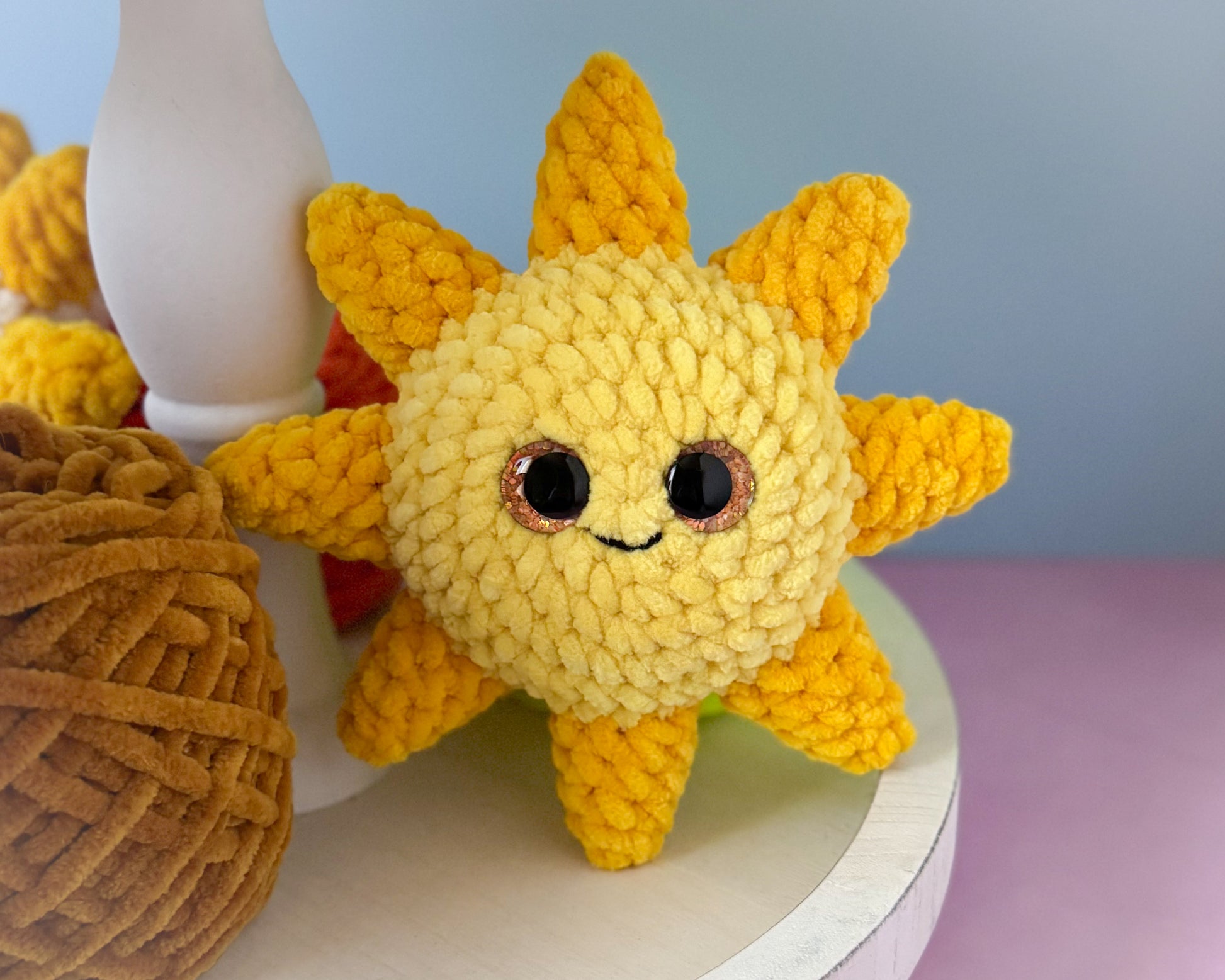 Crocheted sun-shaped toy with a face on a light surface.