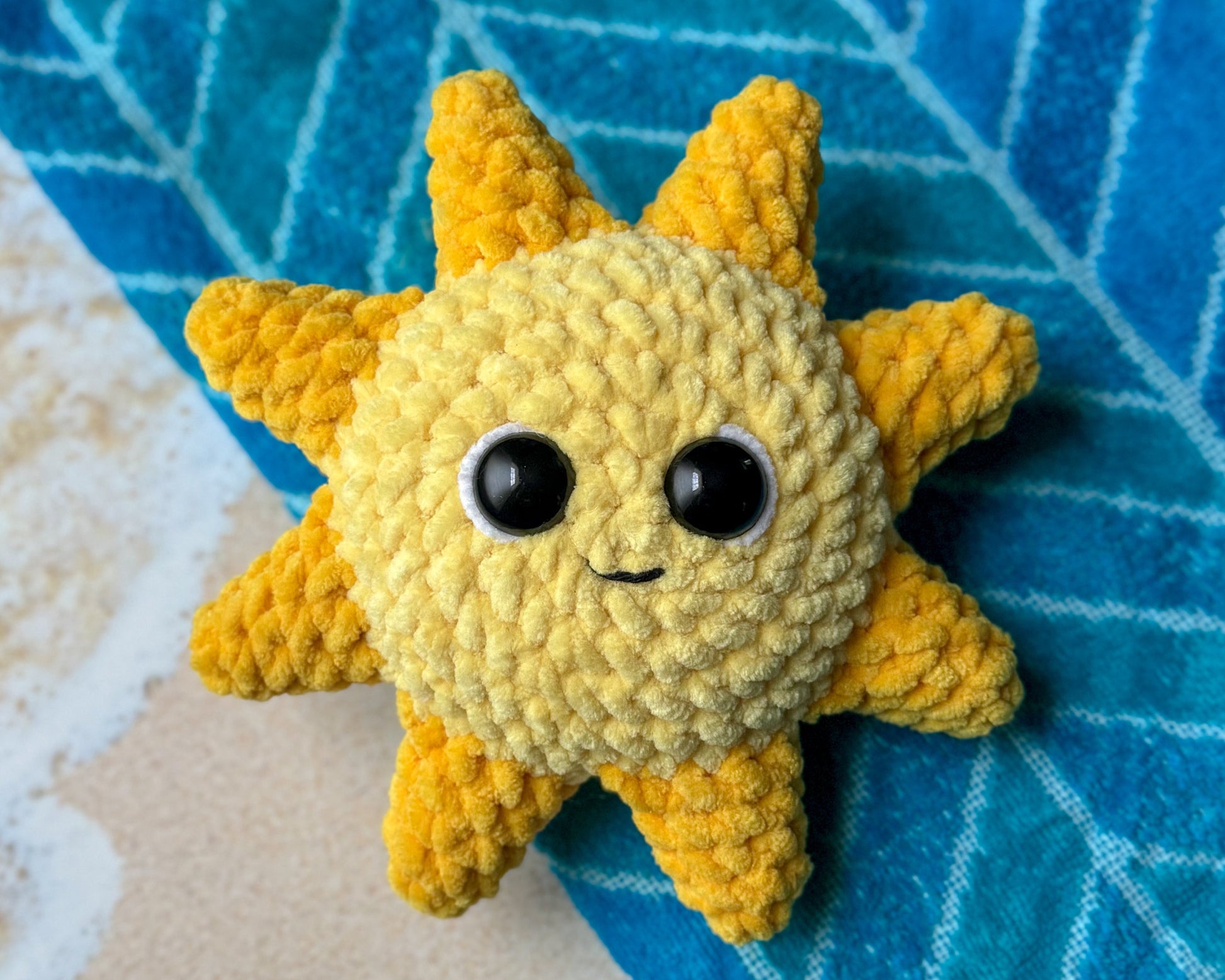 Crocheted sun-shaped toy with black eyes on a blue textured surface.