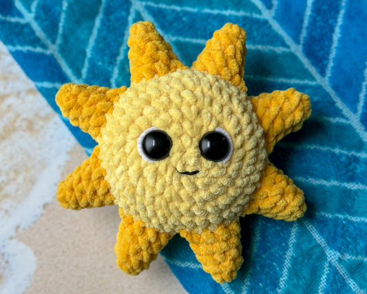 Crocheted sun-shaped toy with black eyes on a blue textured surface.